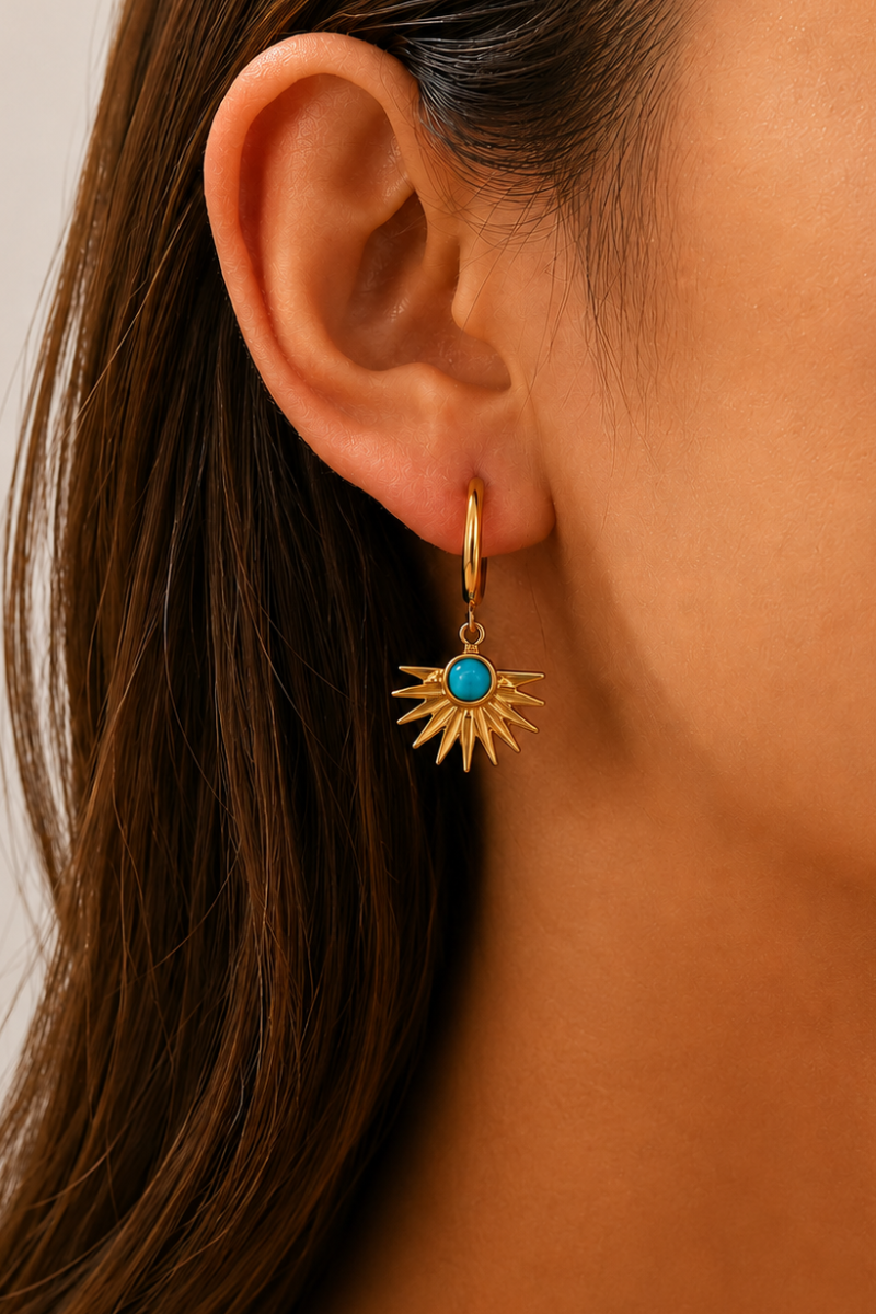 Model draagt de gouden Amalfi sun oorbellen van Fencyjewels met een turquoise steen en opvallend zon-design.
