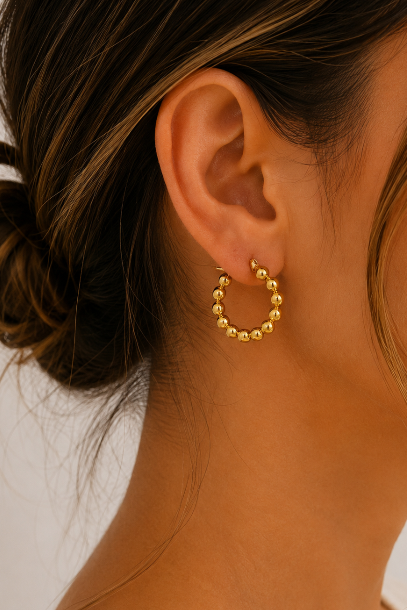Model draagt de gouden Balls oorbellen van Fencyjewels met een speels hoop design van goudkleurige bolletjes.