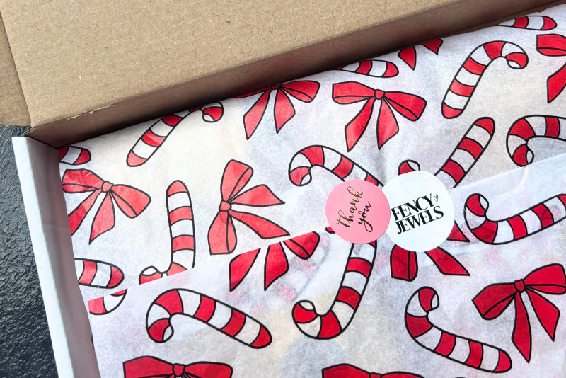 FencyJewels verzenddoos met feestelijk rood-wit cadeaupapier met candy canes, afgesloten met Thank You-sticker en FencyJewels-logo – duurzame sieradenverpakking uit Nederland