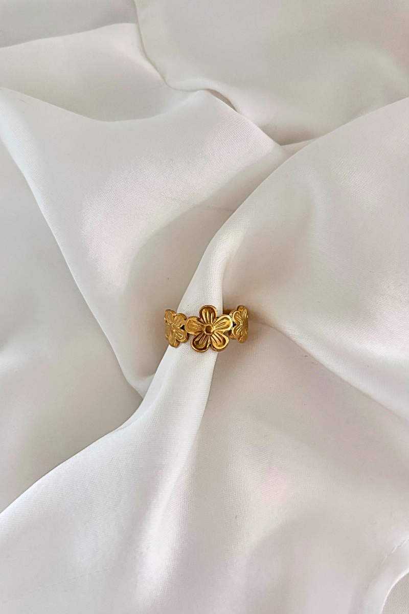 Gouden bloemring van Fencyjewels met gedetailleerde bloemmotieven, elegant gepresenteerd op witte satijnen stof – stijlvolle en verfijnde ring voor een vrouwelijke look.