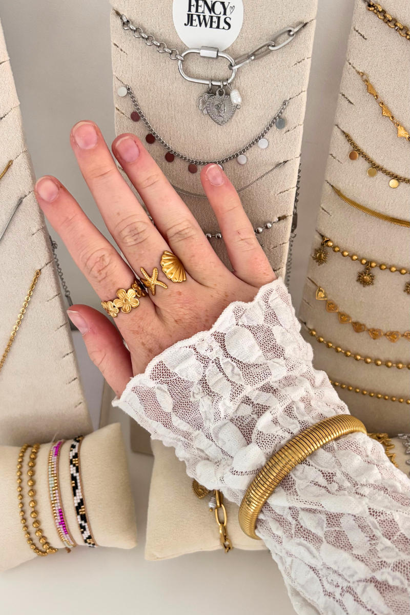 Fencyjewels sieraden – gouden ringen, armbanden en kettingen met elegante details, gedragen met een witte kanten blouse. Luxe en trendy jewelry display met hand en sieraden