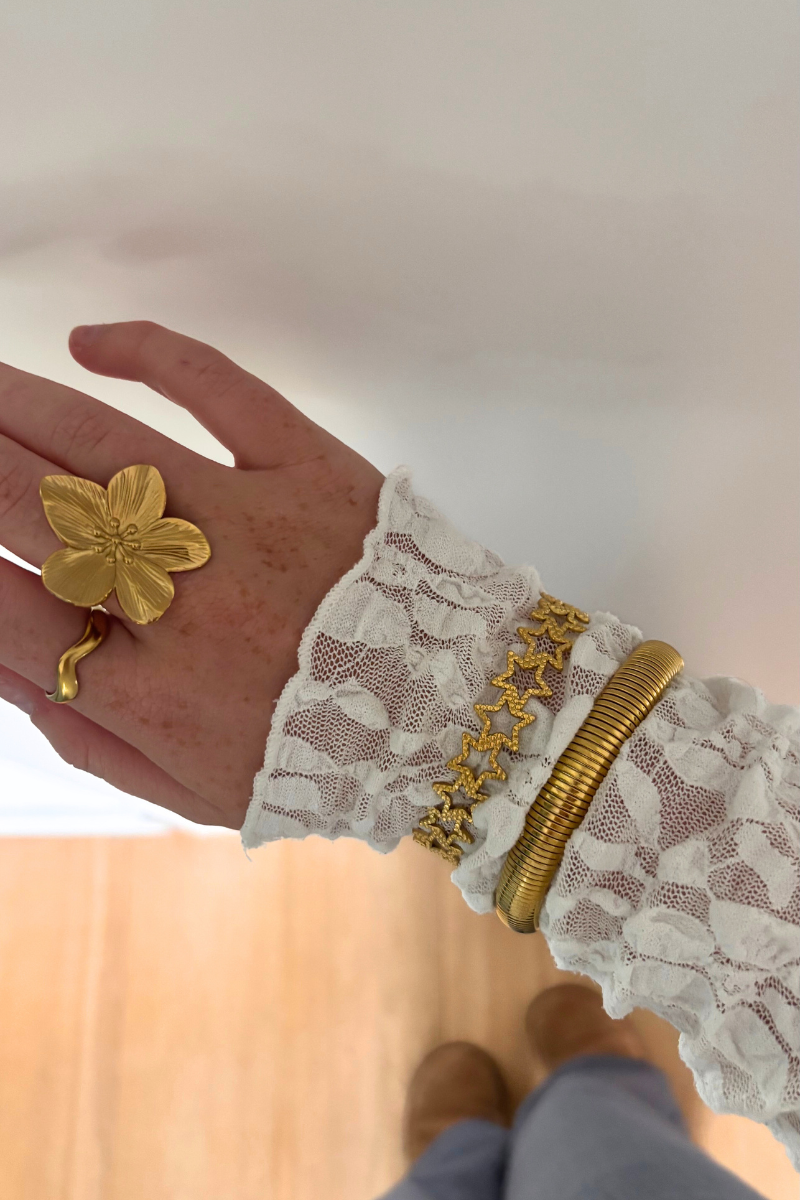 Gouden Fencyjewels armbanden en bloemring gedragen met een witte kanten blouse – stijlvolle en elegante dames sieraden in een luxueuze gouden afwerking.