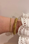 Gouden armbanden set van FencyJewels – een minimalistische dunne armband gecombineerd met een brede goudkleurige snake-armband, gedragen aan de pols