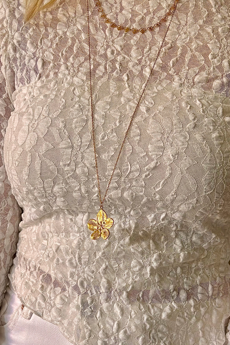 Gouden bloemketting van Fencyjewels met fijn patroon, gedragen op een witte kanten top voor een elegante en vrouwelijke look.