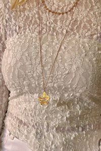 Gouden bloemketting van Fencyjewels met fijn patroon, gedragen op een witte kanten top voor een elegante en vrouwelijke look.