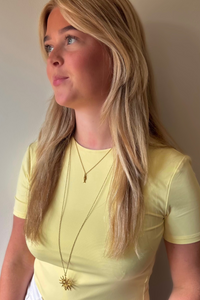Fencyjewels gouden kettingen met zon en vis hanger, gedragen bij een pastelgele top. Trendy layered necklace look met zomerse sieraden van Fencyjewels.