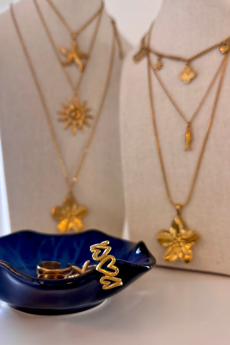 Gouden sieraden van Fencyjewels met bloem-, zon- en hartontwerpen, uitgestald op sieradenbustes met blauwe sieradenschaal op de voorgrond.