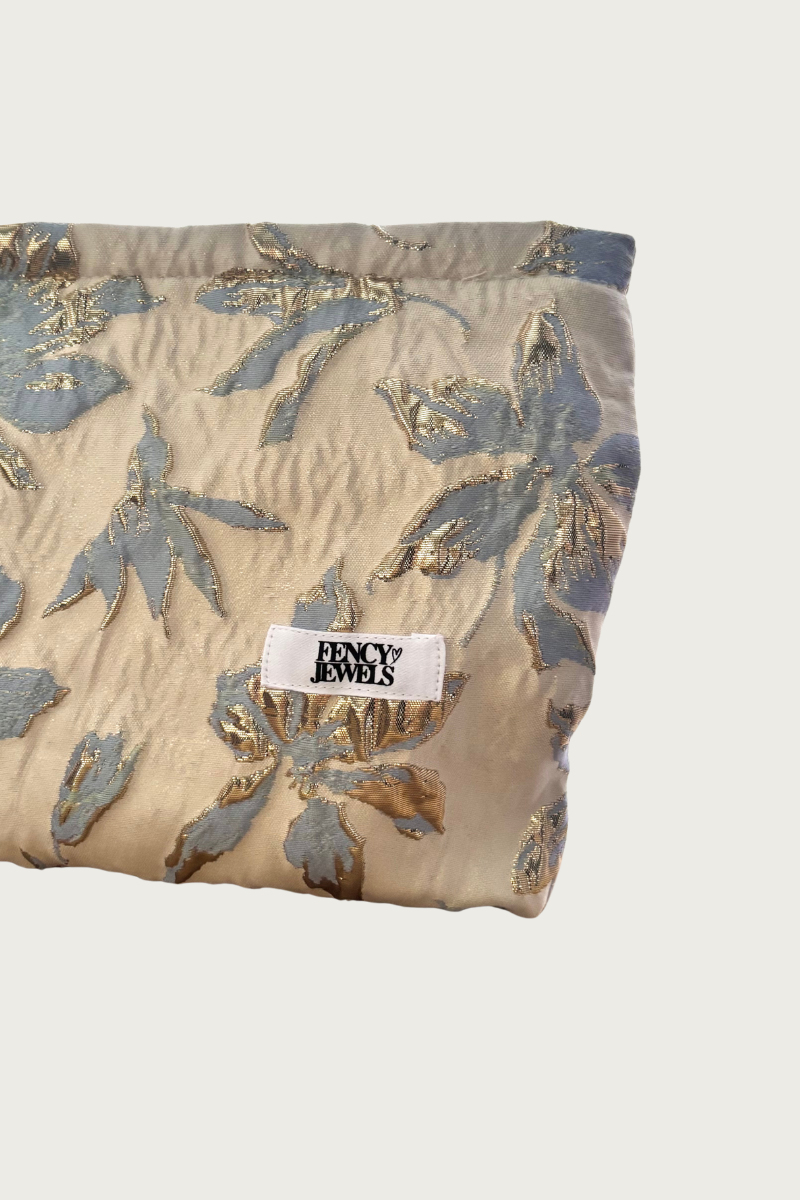 Luxe sieradentasje van Fencyjewels met lichtblauwe en gouden bloemenborduursels en wit logo-label op een beige achtergrond.
