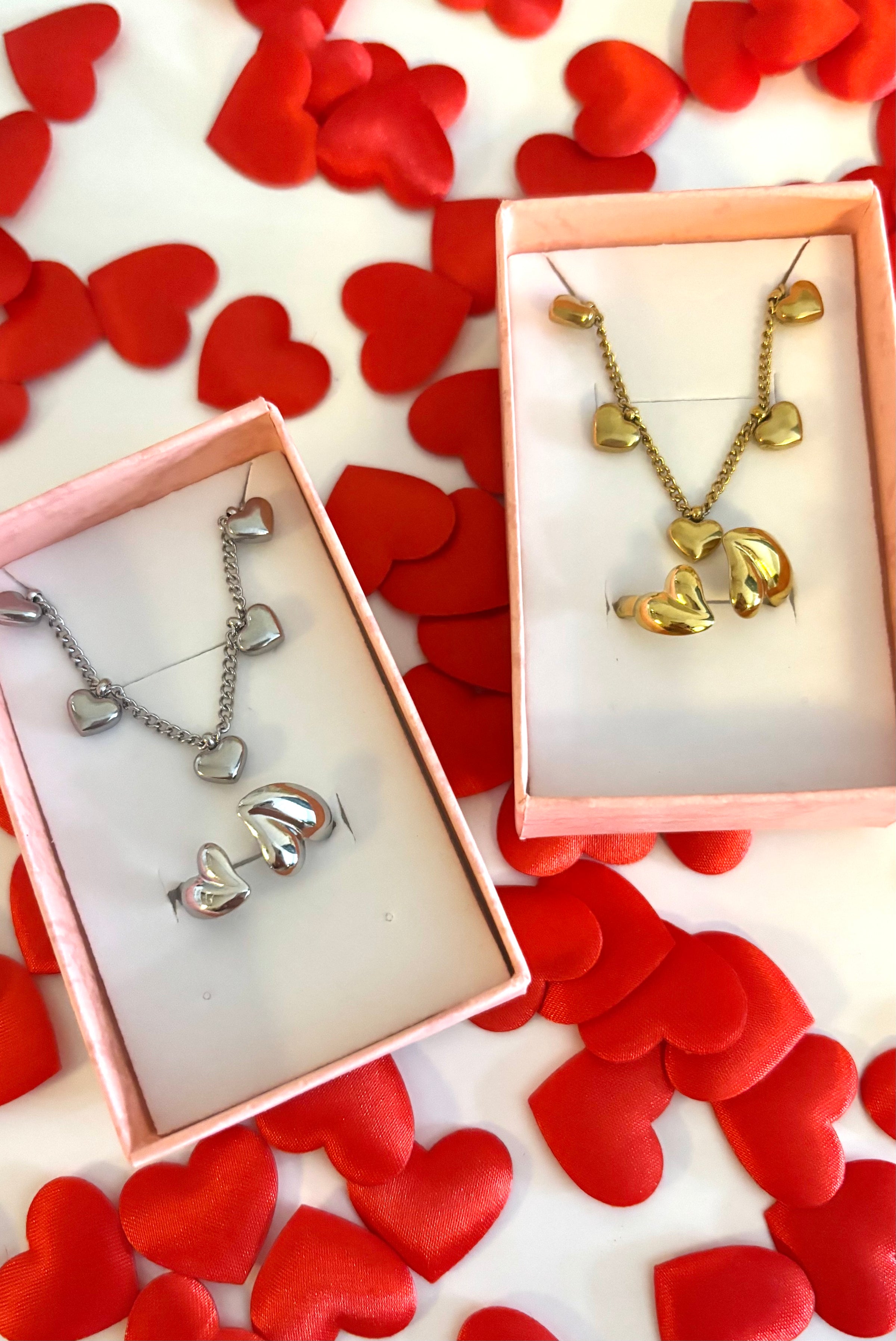 Close-up van gouden sieraden in doosje van Fencyjewels, omringd door hartjes. Luxe valentijnscadeau met fijne details.