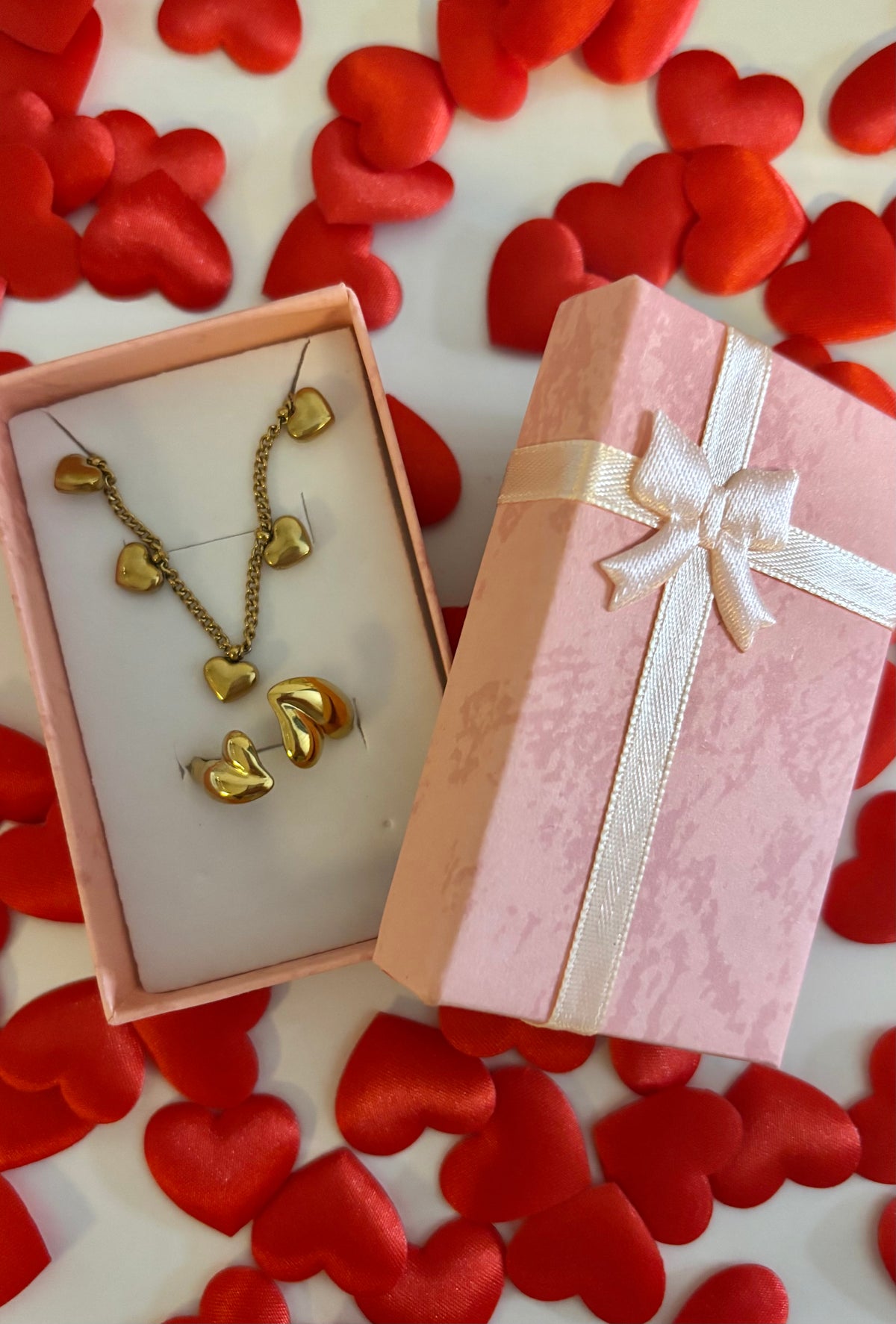 Valentijnscadeau van Fencyjewels met gouden sieraden in luxe doosje, omringd door rode hartjes. Perfect cadeau voor haar, stainless steel en waterproof.